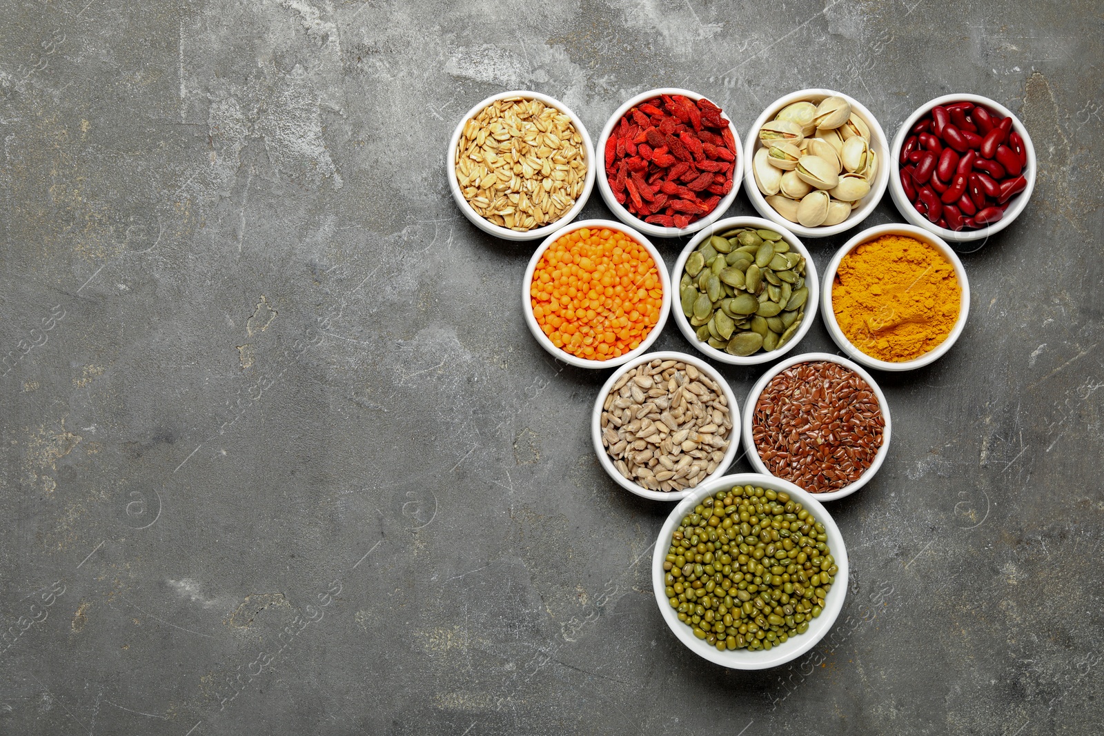 Photo of Different superfoods in bowls on grey table, flat lay. Space for text