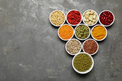 Photo of Different superfoods in bowls on grey table, flat lay. Space for text