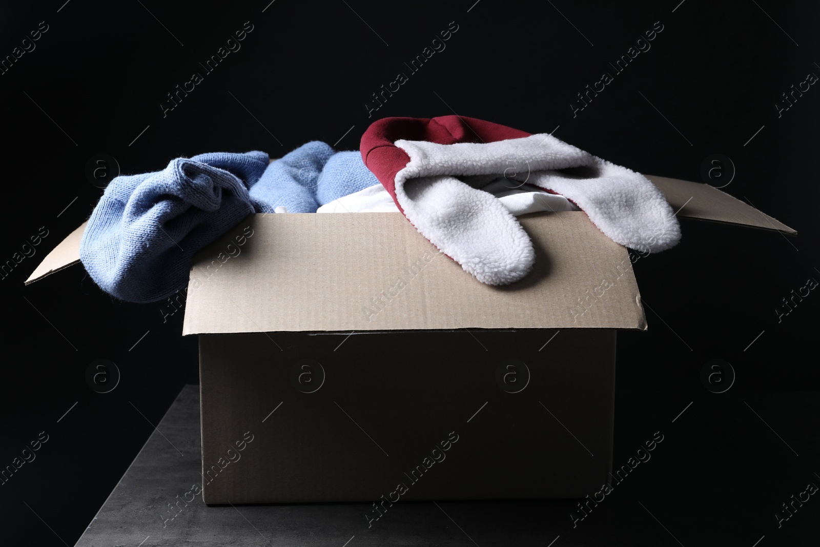 Photo of Different used clothes in box on dark background