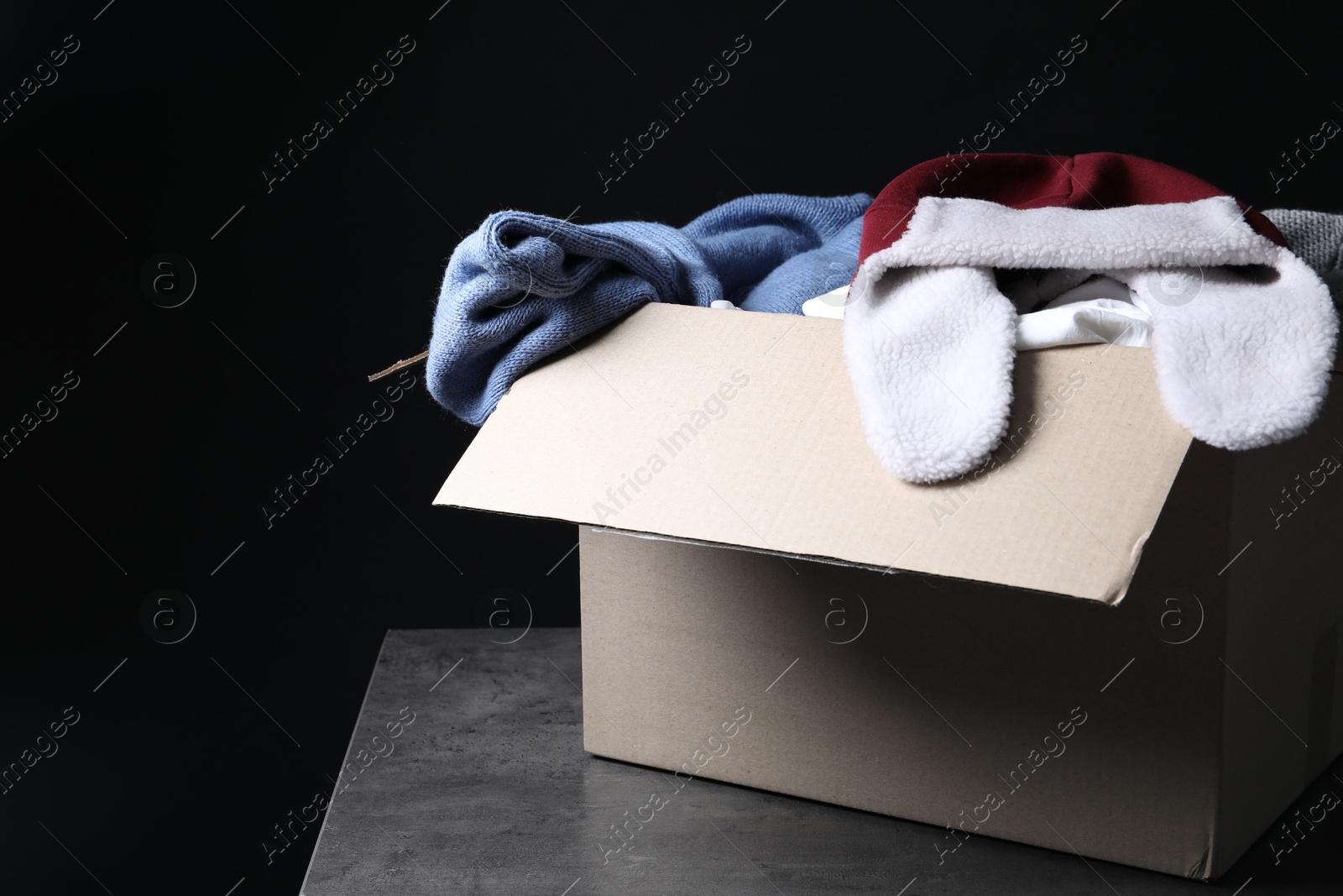 Photo of Different used clothes in box on dark background