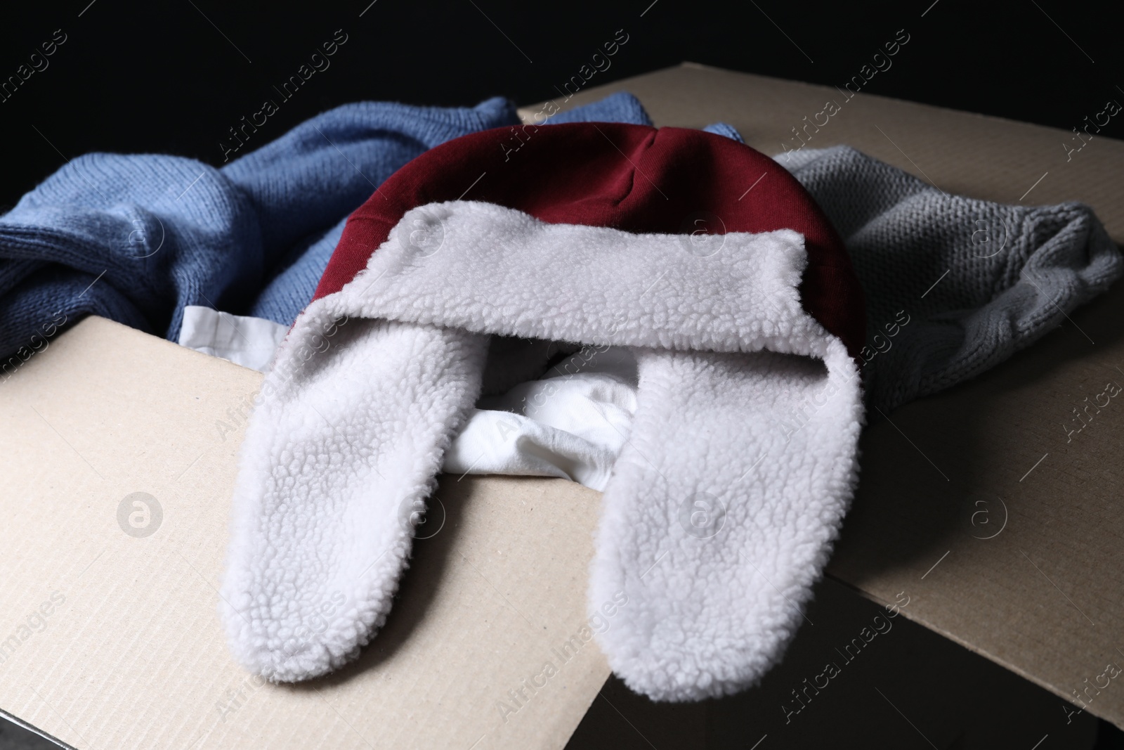 Photo of Different used clothes in box on dark background, closeup