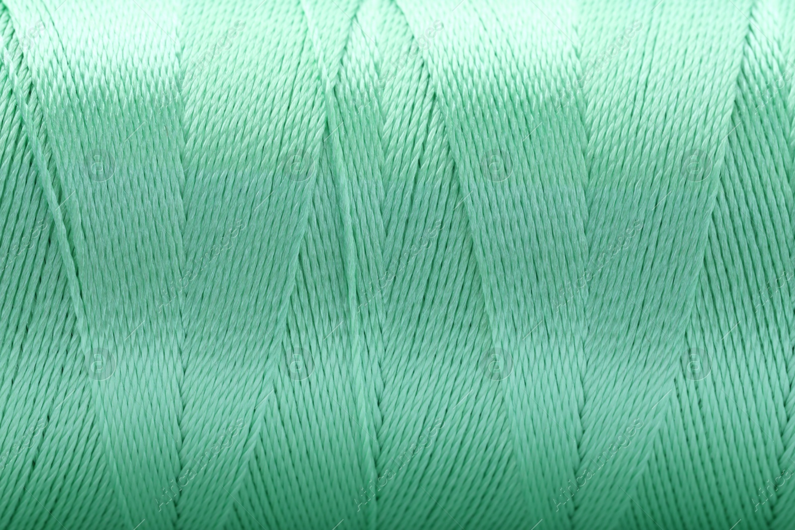 Photo of Beautiful light green sewing thread as background, closeup