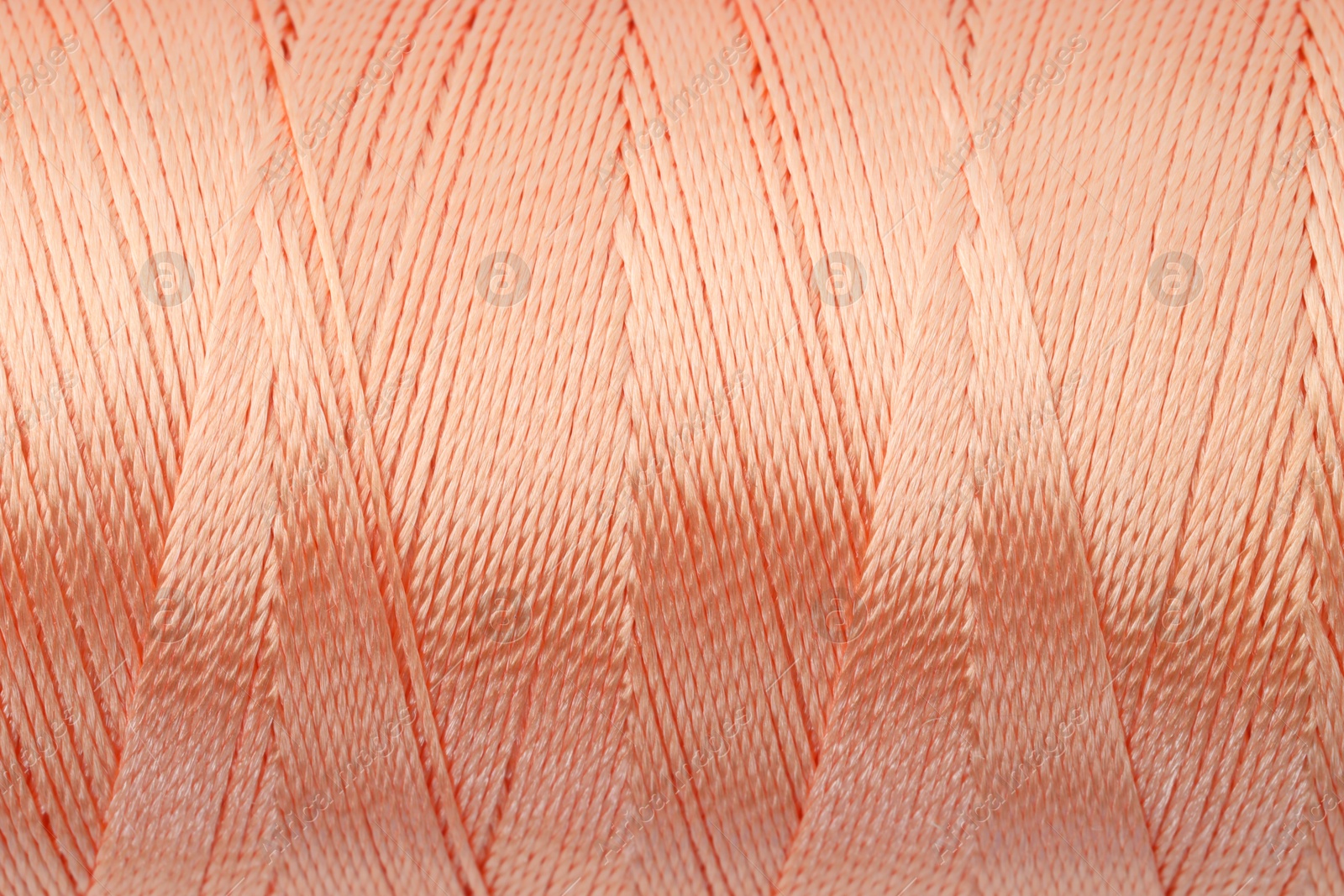 Photo of Beautiful peach sewing thread as background, closeup