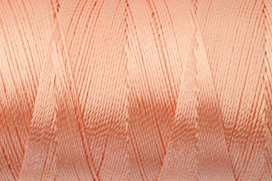 Photo of Beautiful peach sewing thread as background, closeup