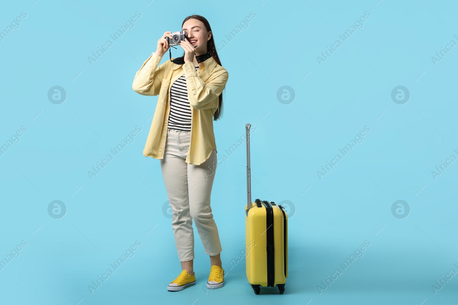 Photo of Woman with vintage camera and suitcase on light blue background