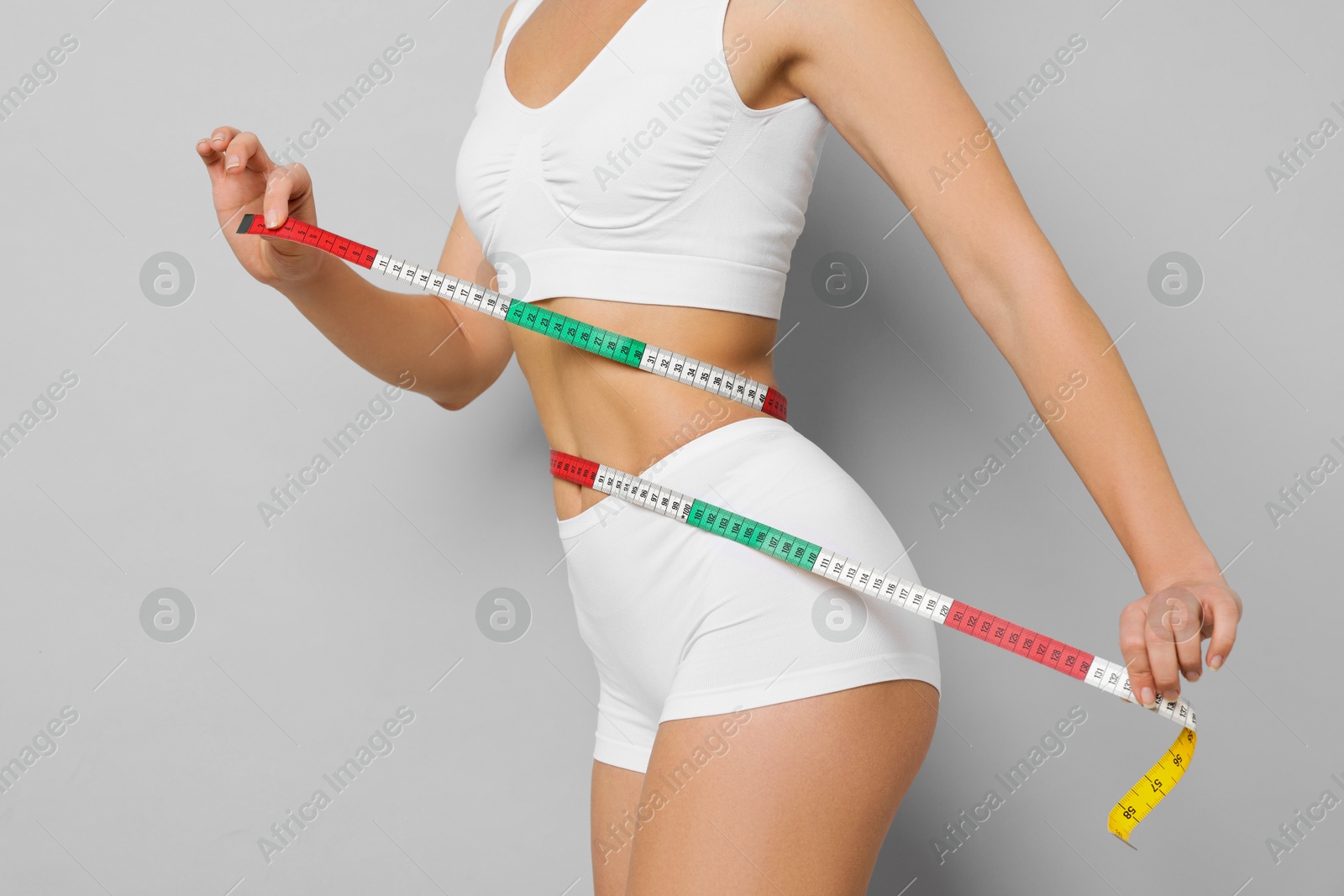 Photo of Weight loss. Woman measuring her slim waist with tape on light grey background, closeup