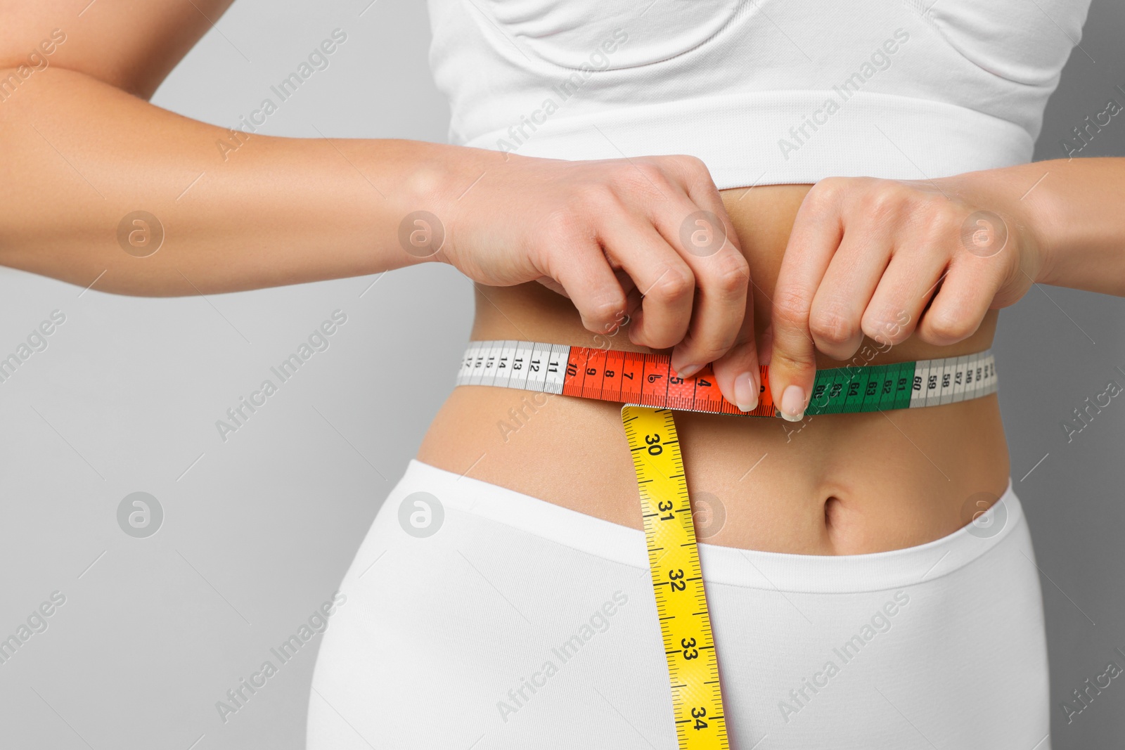 Photo of Weight loss. Woman measuring her slim waist with tape on light grey background, closeup