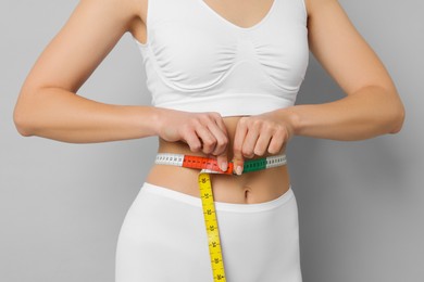 Photo of Weight loss. Woman measuring her slim waist with tape on light grey background, closeup