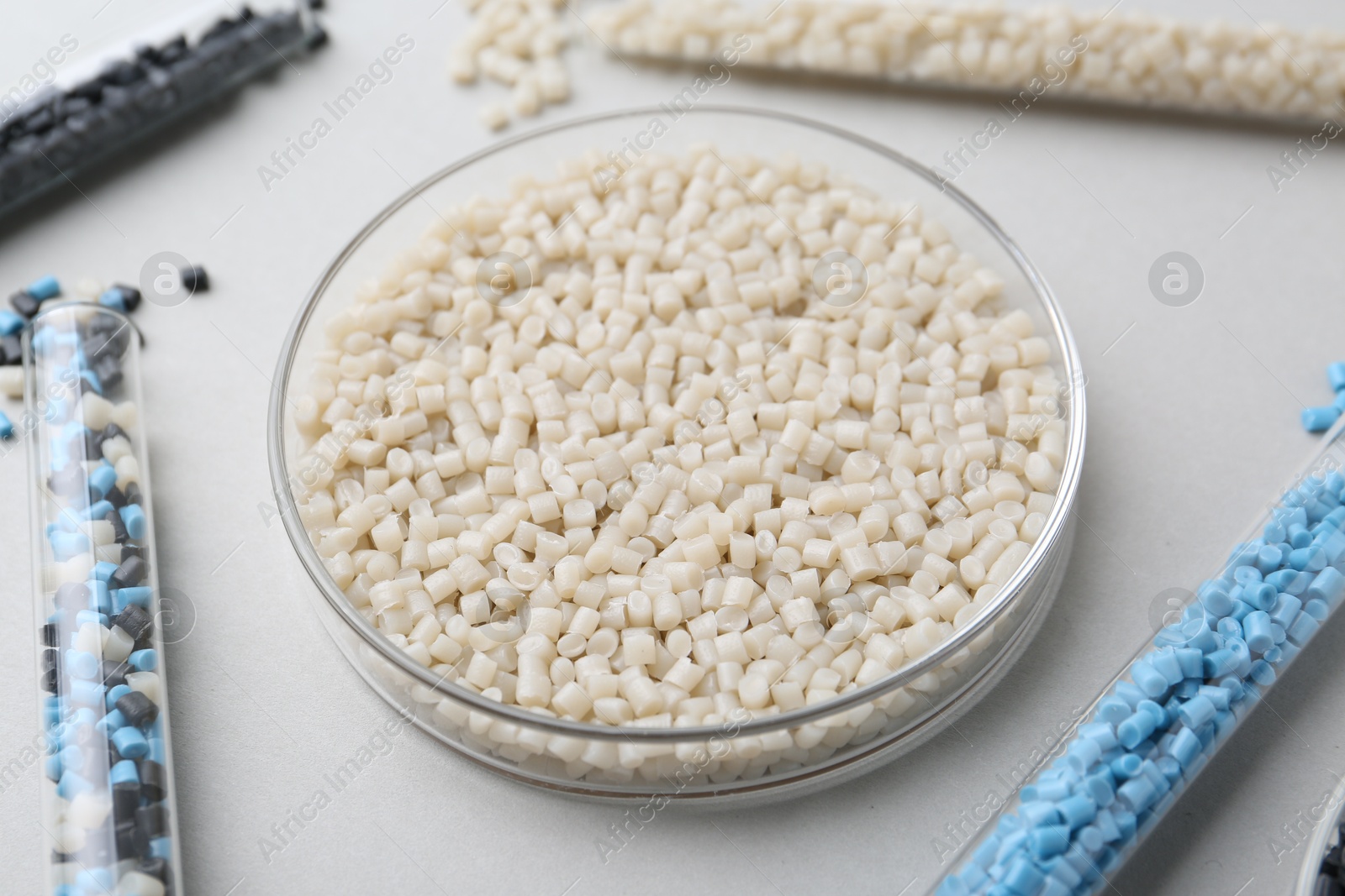 Photo of Colorful plastic granules in petri dish and test tubes on gray background, closeup