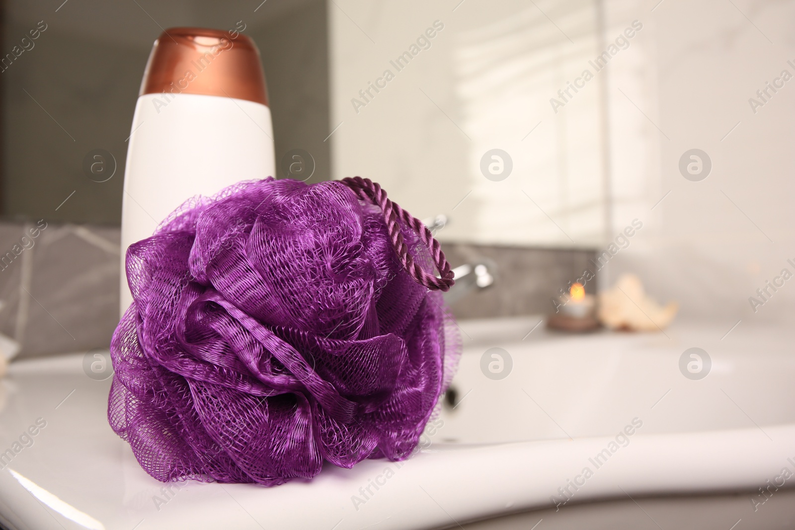 Photo of Purple shower puff and bottle of body wash gel on sink in bathroom, space for text