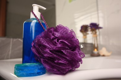 Photo of Purple shower puff and cosmetic products on sink in bathroom