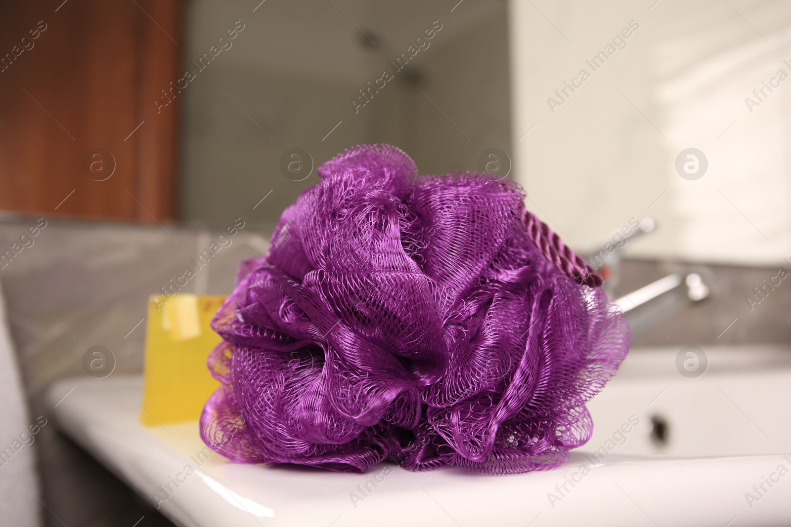 Photo of Purple shower puff and soap on sink in bathroom, closeup