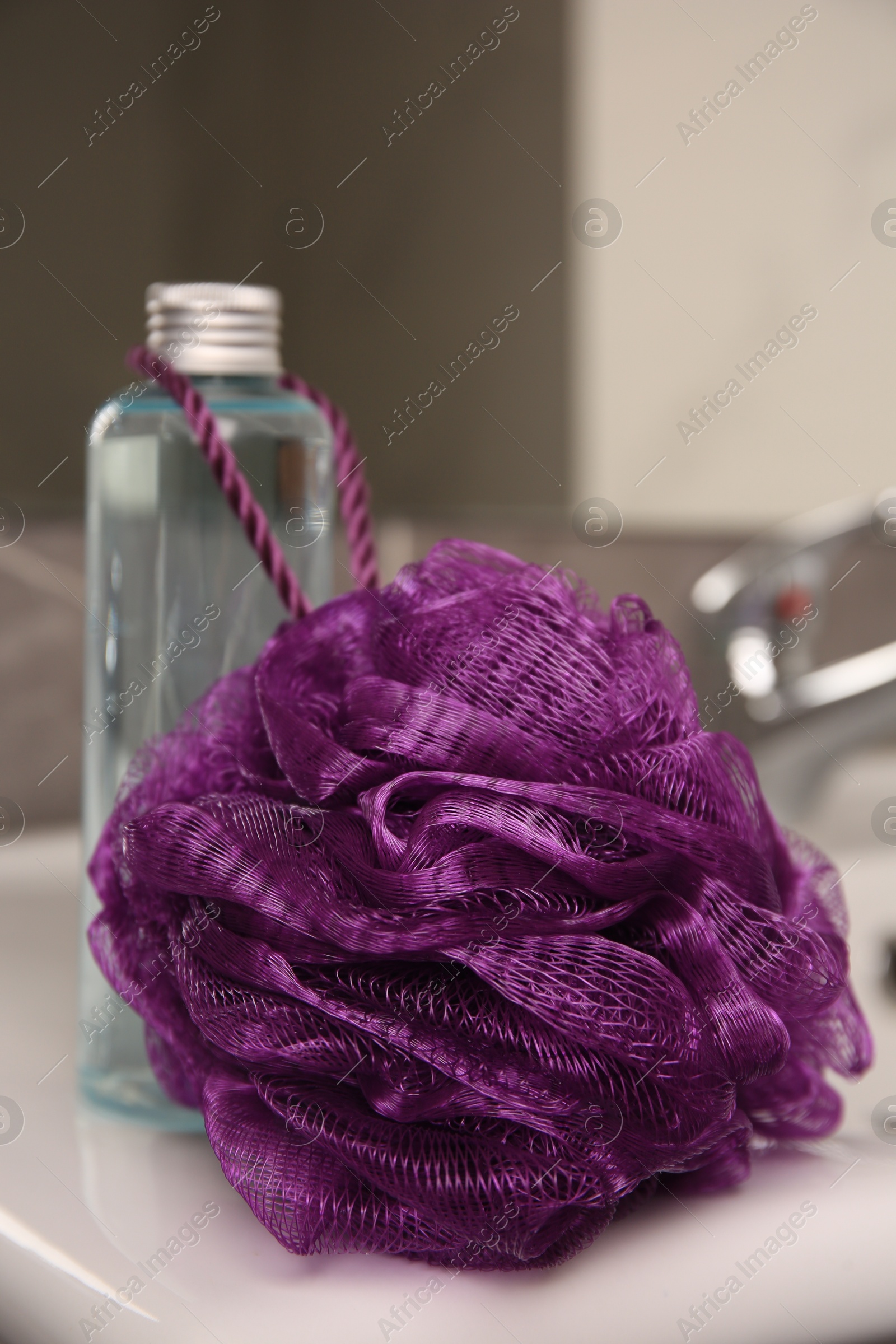 Photo of Purple shower puff and bottle of body wash gel on sink in bathroom, closeup