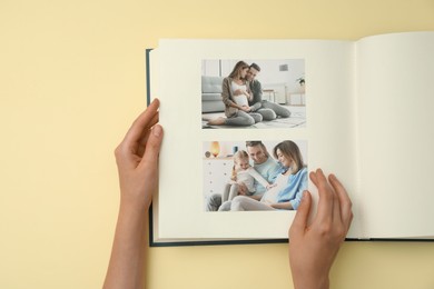 Photo of Woman looking at family photos in photo album on beige background, top view