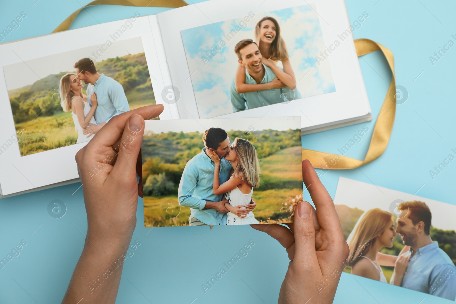 Photo of Woman with open photo album and different photos on light blue background, top view