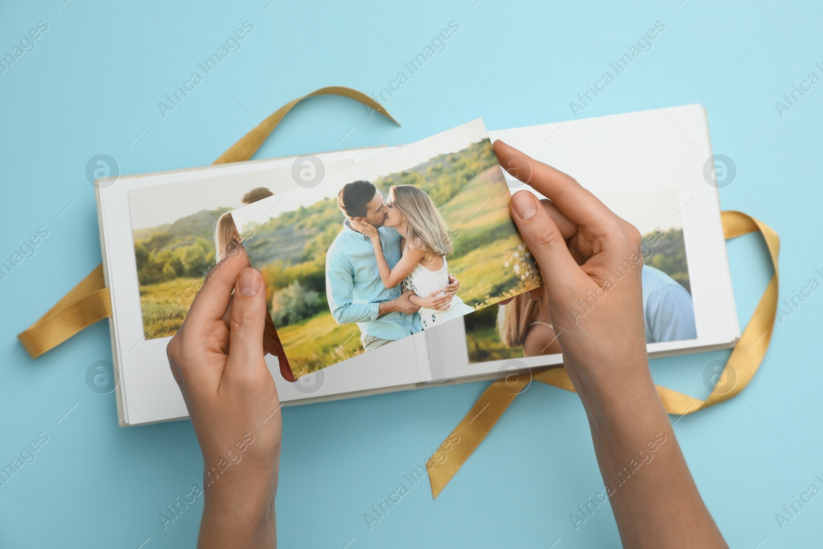 Photo of Woman looking at family photos in photo album on light blue background, top view