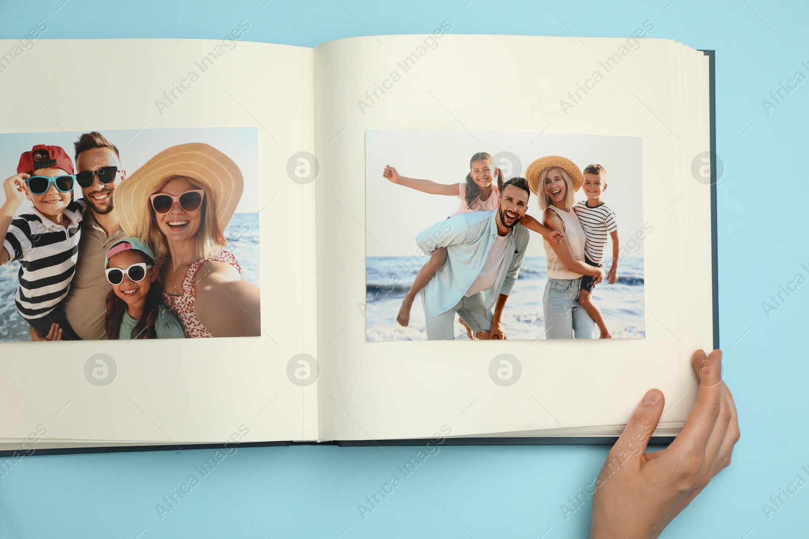 Photo of Woman looking at family photos in photo album on light blue background, top view