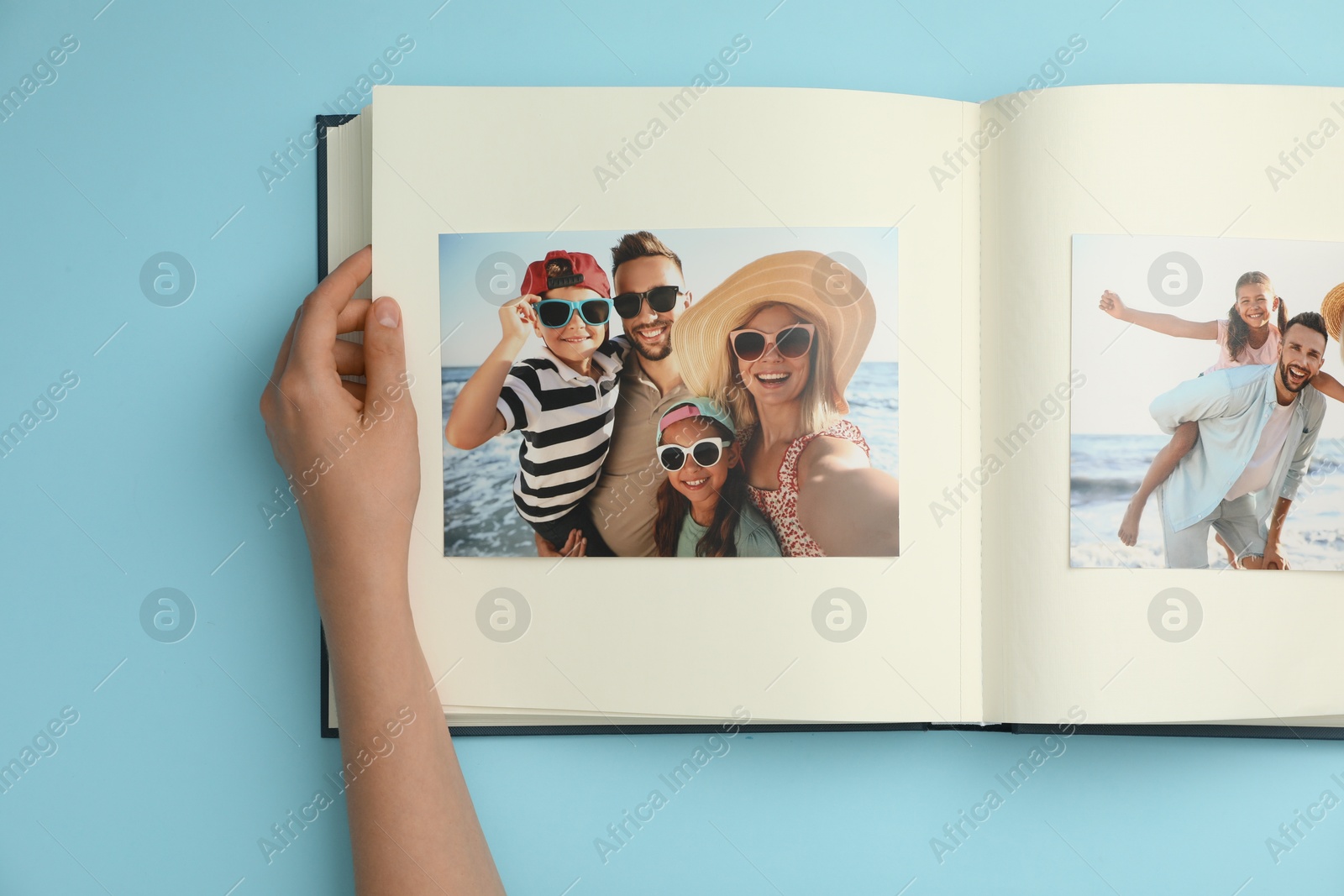 Photo of Woman looking at family photos in photo album on light blue background, top view