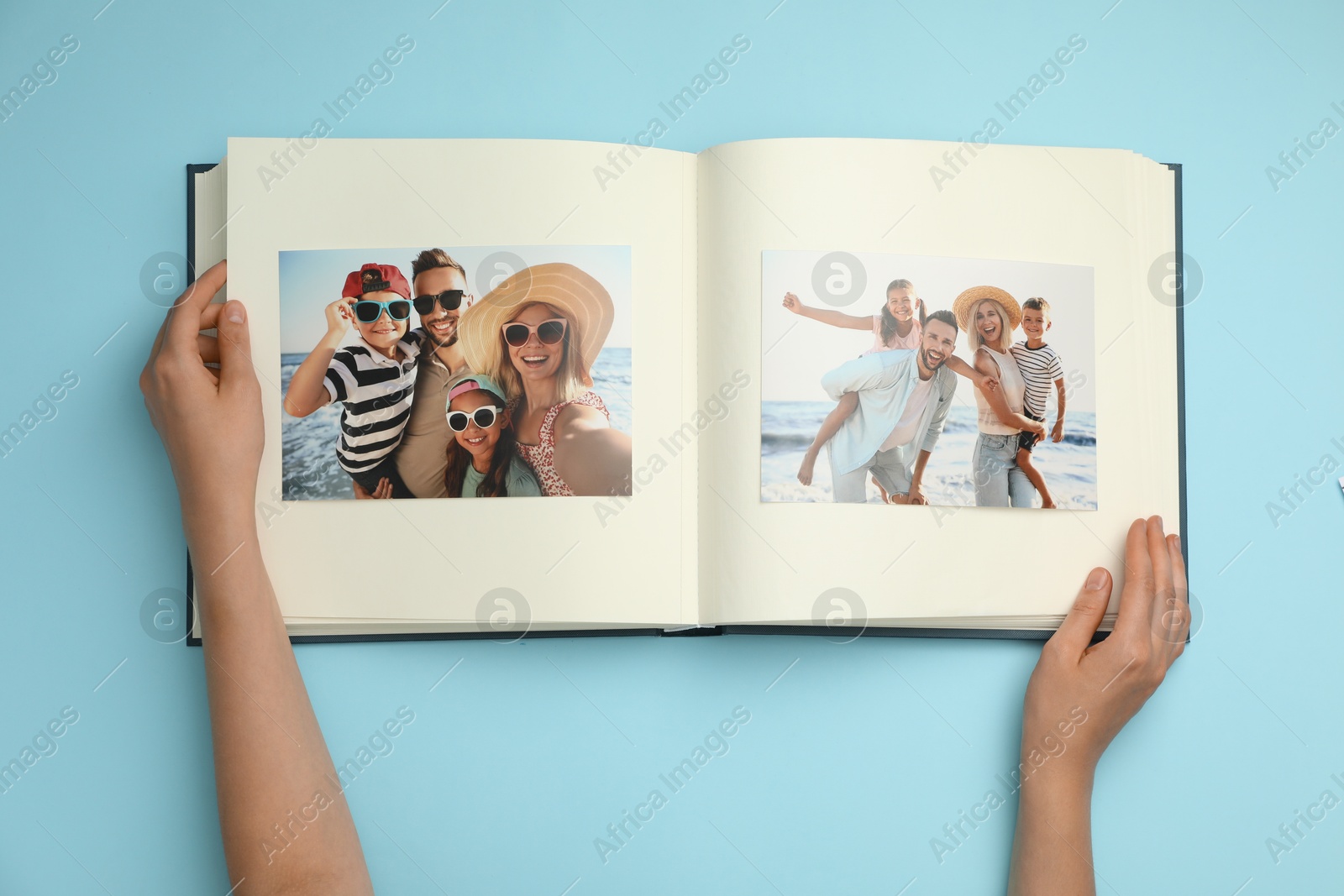 Photo of Woman looking at family photos in photo album on light blue background, top view