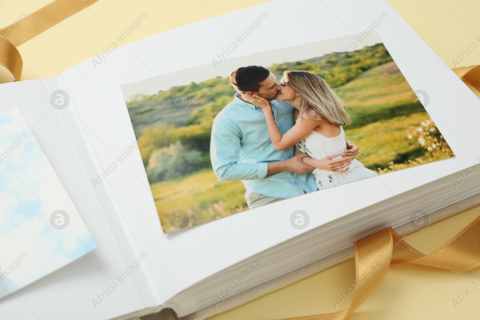 Photo of Open photo album and ribbon on beige background, closeup