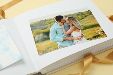 Photo of Open photo album and ribbon on beige background, closeup