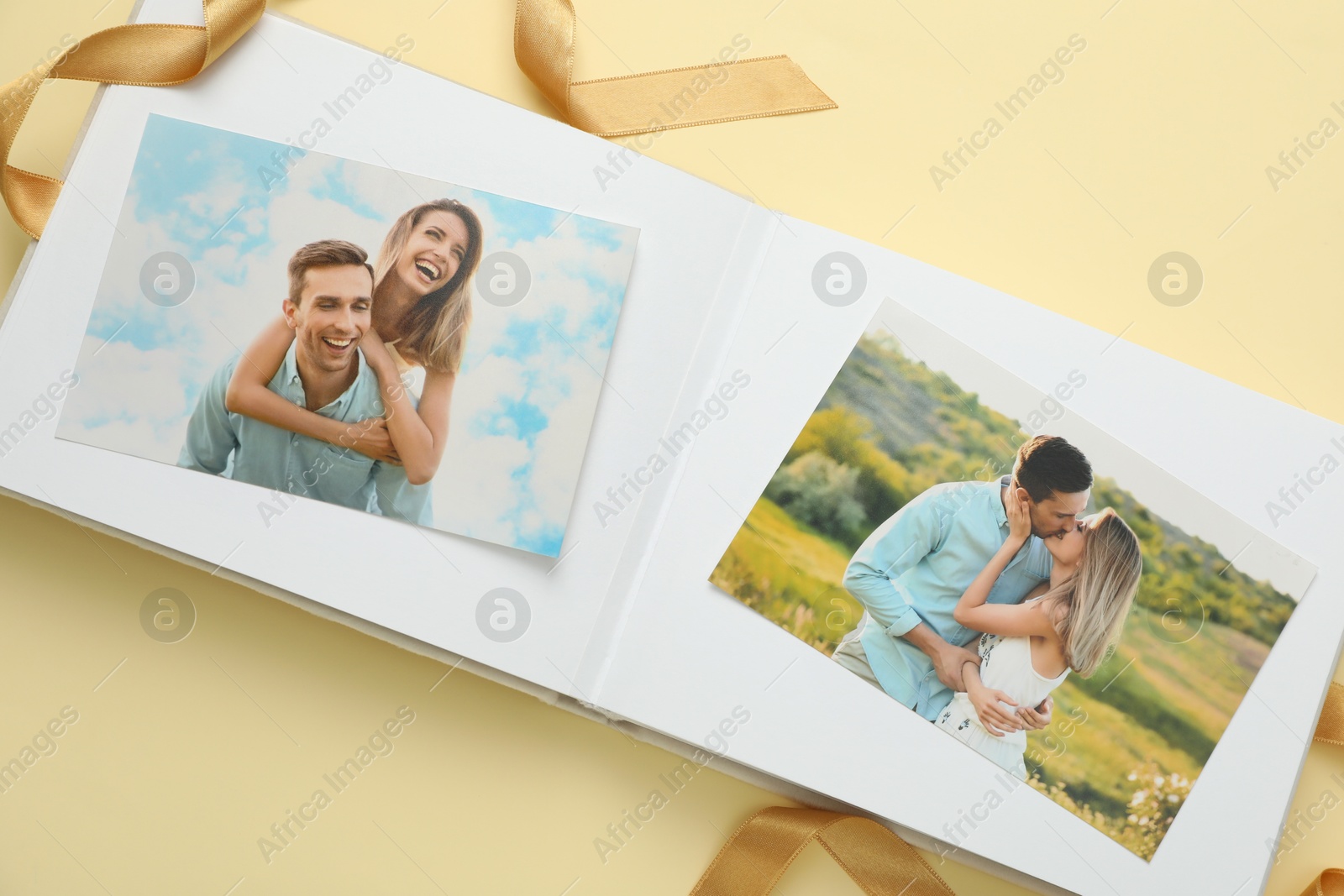 Photo of Open photo album with photos and ribbon on beige background, top view