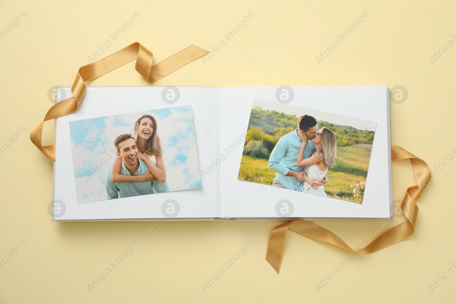 Photo of Open photo album with photos and ribbon on beige background, top view