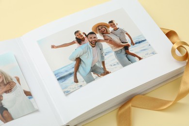 Photo of Open photo album with photos and ribbon on beige background, closeup