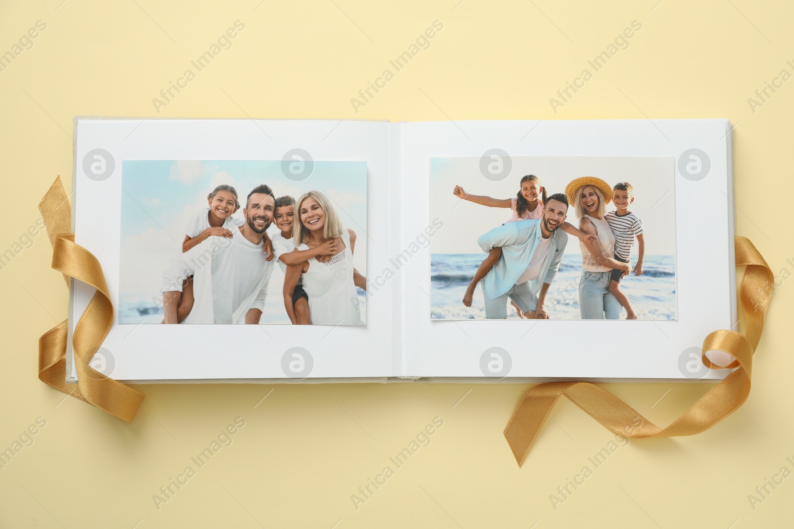 Photo of Open photo album with photos and ribbon on beige background, top view