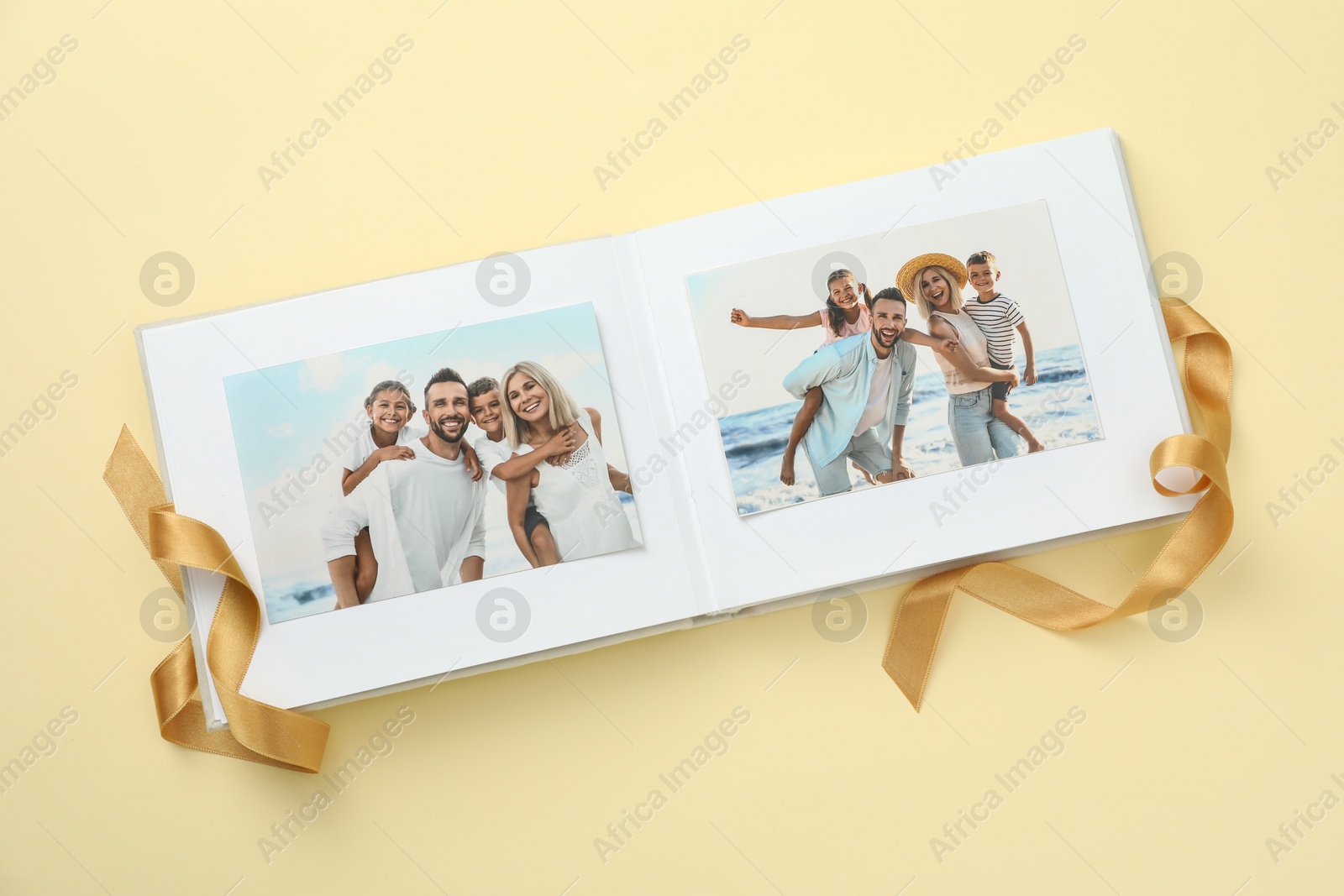 Photo of Open photo album with photos and ribbon on beige background, top view