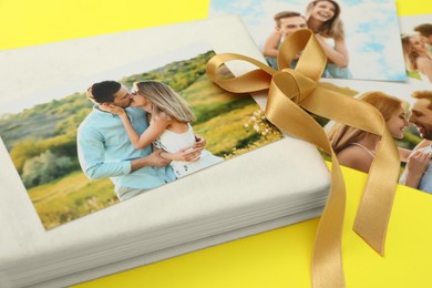 Photo of Photo album with different photos and ribbon on yellow background, closeup