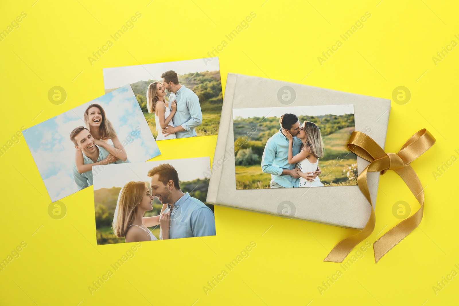 Photo of Photo album with different photos and ribbon on yellow background, top view