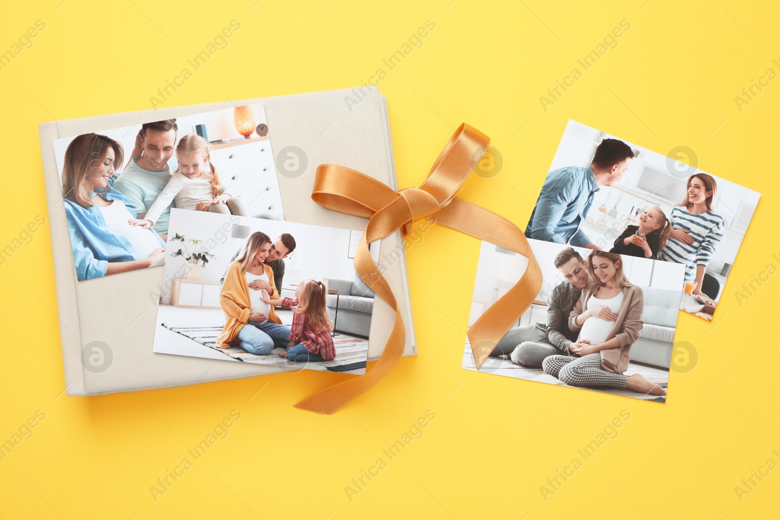 Photo of Photo album with different photos and ribbon on yellow background, top view