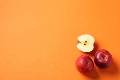 Photo of Whole and cut fresh red apples on orange background, top view. Space for text