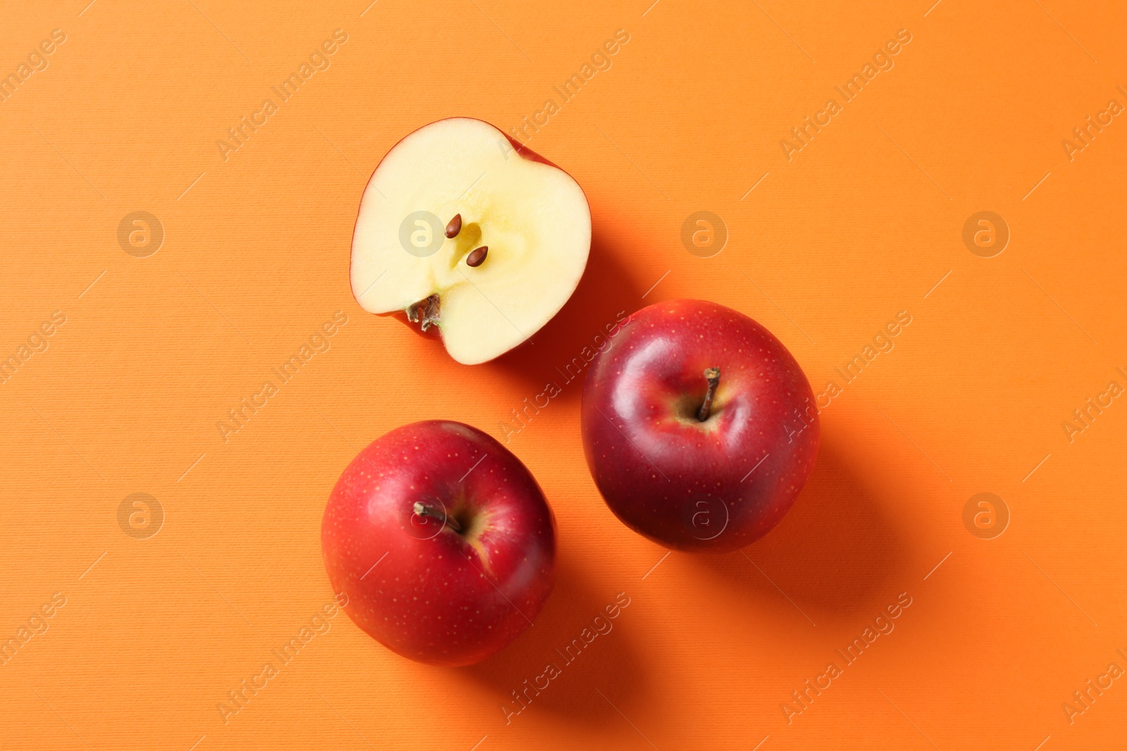 Photo of Whole and cut fresh red apples on orange background, top view