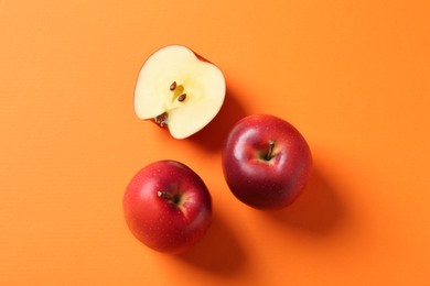 Whole and cut fresh red apples on orange background, top view