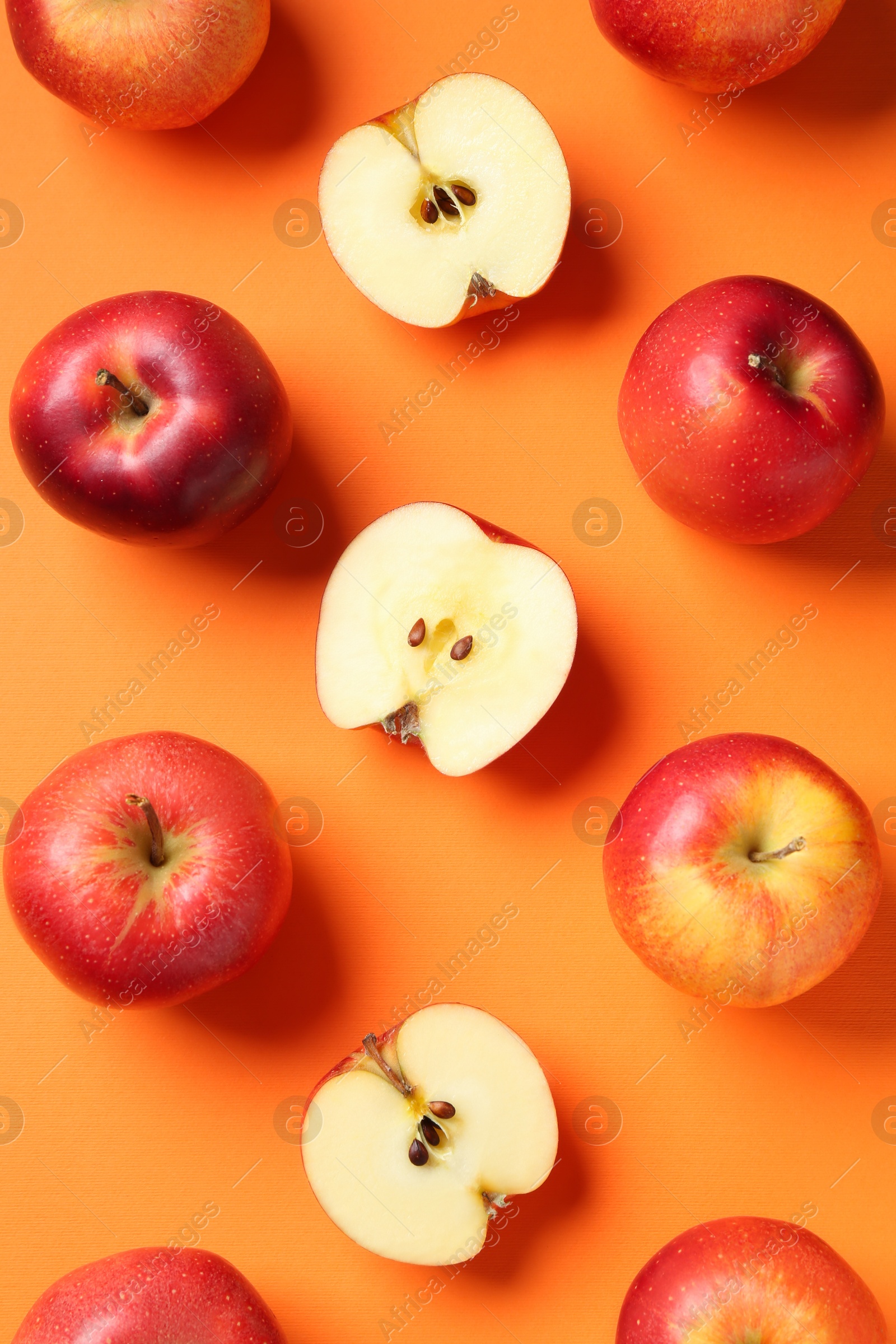 Photo of Whole and cut fresh red apples on orange background, flat lay