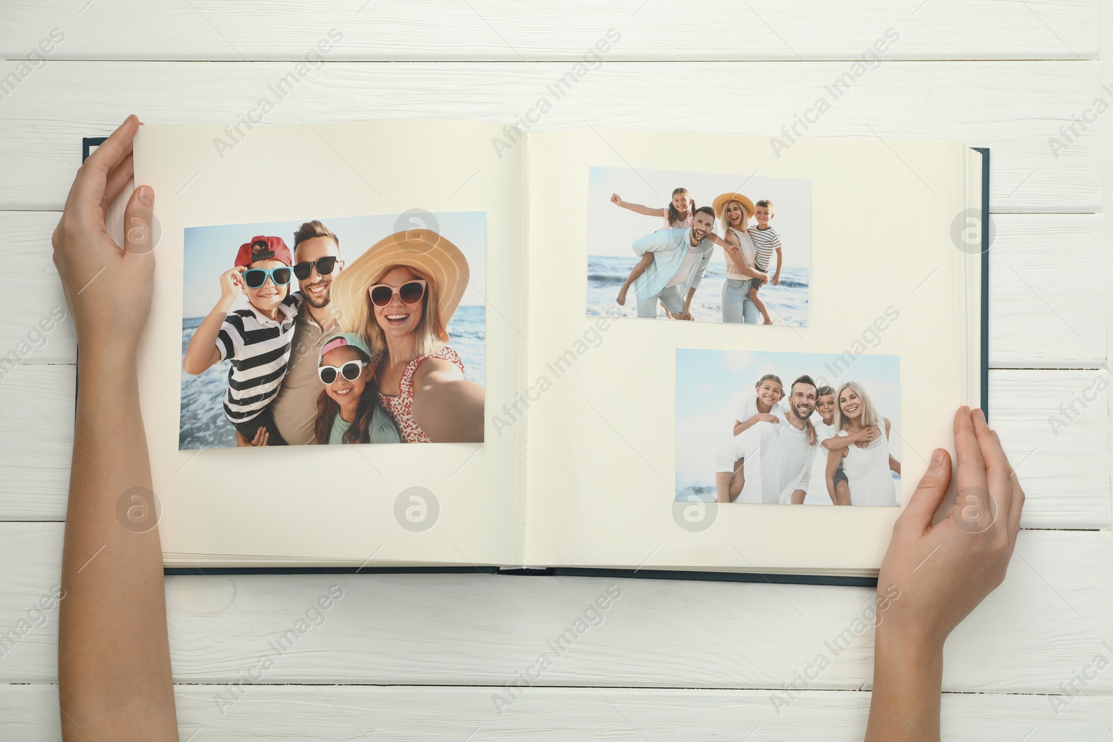 Photo of Woman with different photos in open photo album at white wooden table, top view