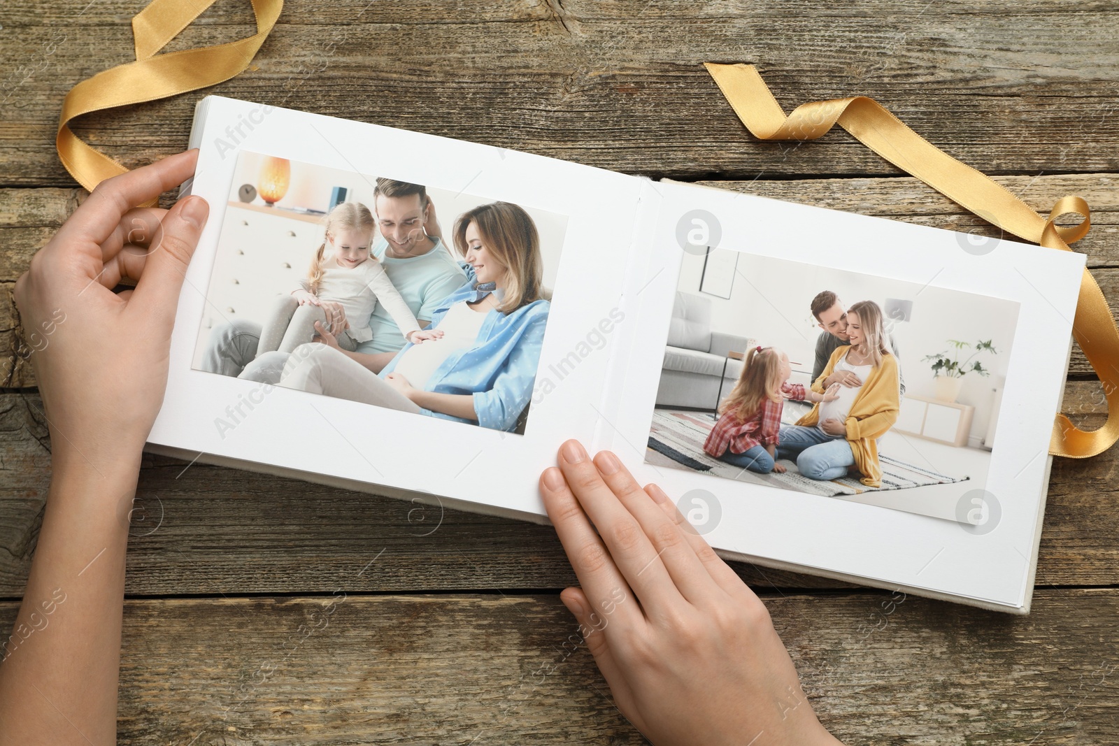 Photo of Woman with different photos in open photo album at wooden table, top view