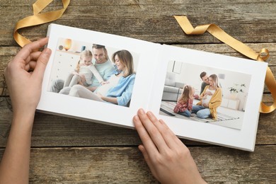 Photo of Woman with different photos in open photo album at wooden table, top view