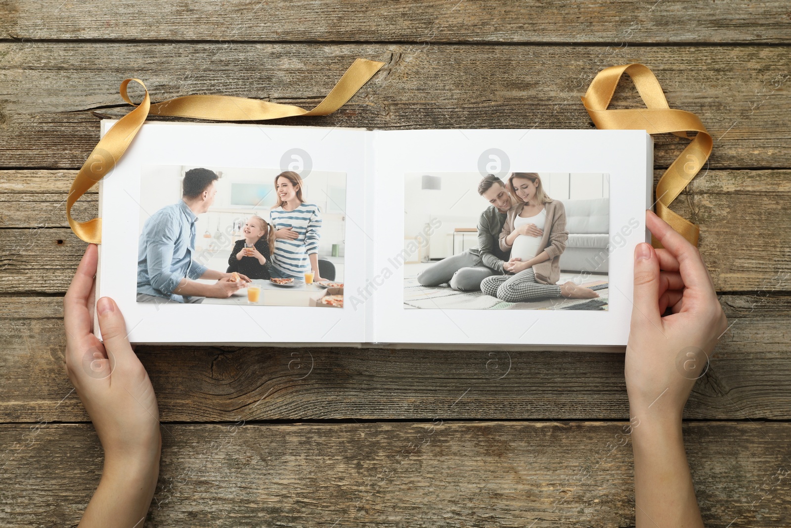 Photo of Woman with different photos in open photo album at wooden table, top view