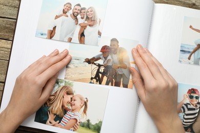 Photo of Woman with different photos in open photo album at wooden table, top view