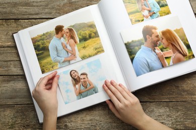 Photo of Woman with different photos in open photo album at wooden table, top view