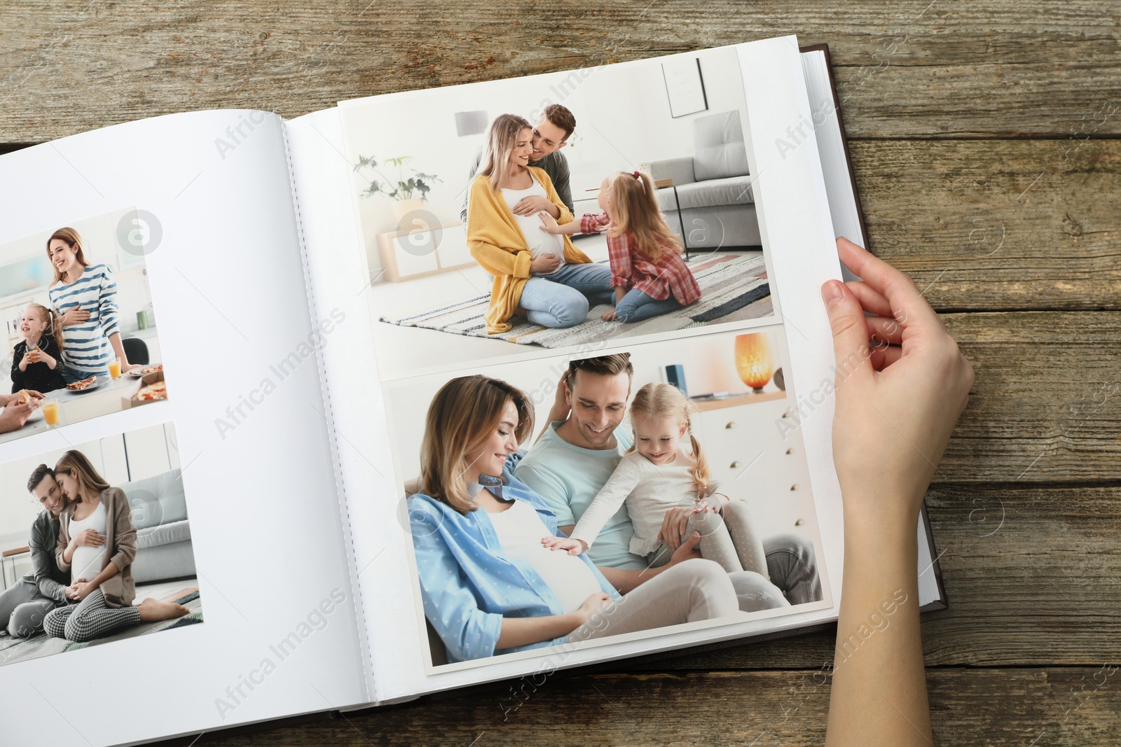 Photo of Woman with different photos in open photo album at wooden table, top view