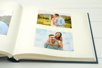 Photo of Different photos in open photo album on white wooden table, closeup