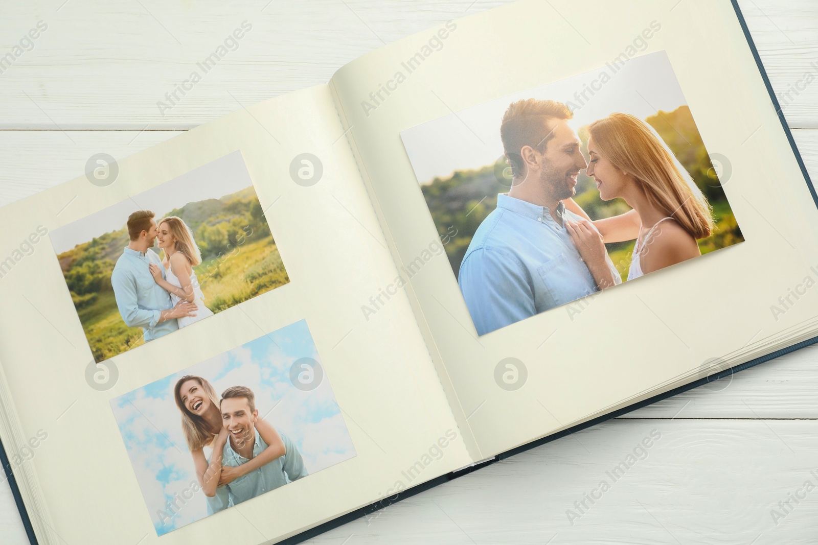 Photo of Different photos in open photo album on white wooden table, top view