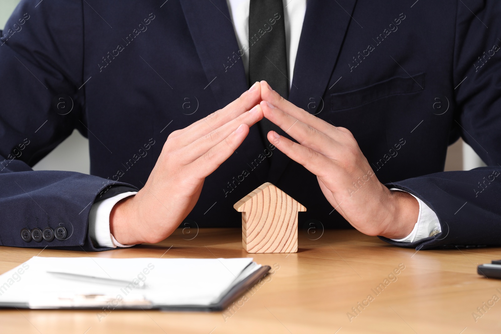 Photo of Property insurance. Real estate agent protecting house figure at table, closeup