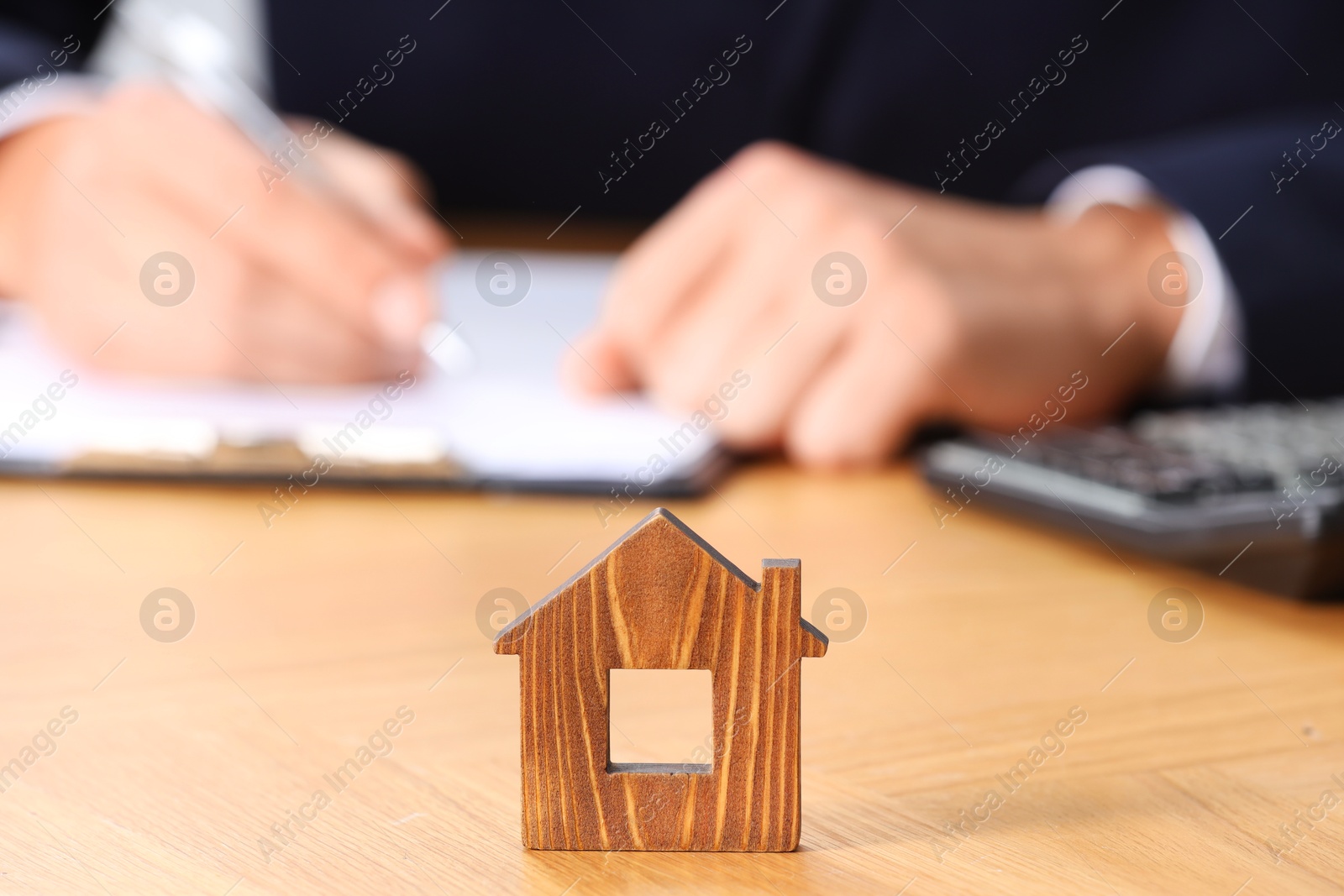 Photo of Property insurance. Real estate agent working at table indoors, focus on wooden house figure