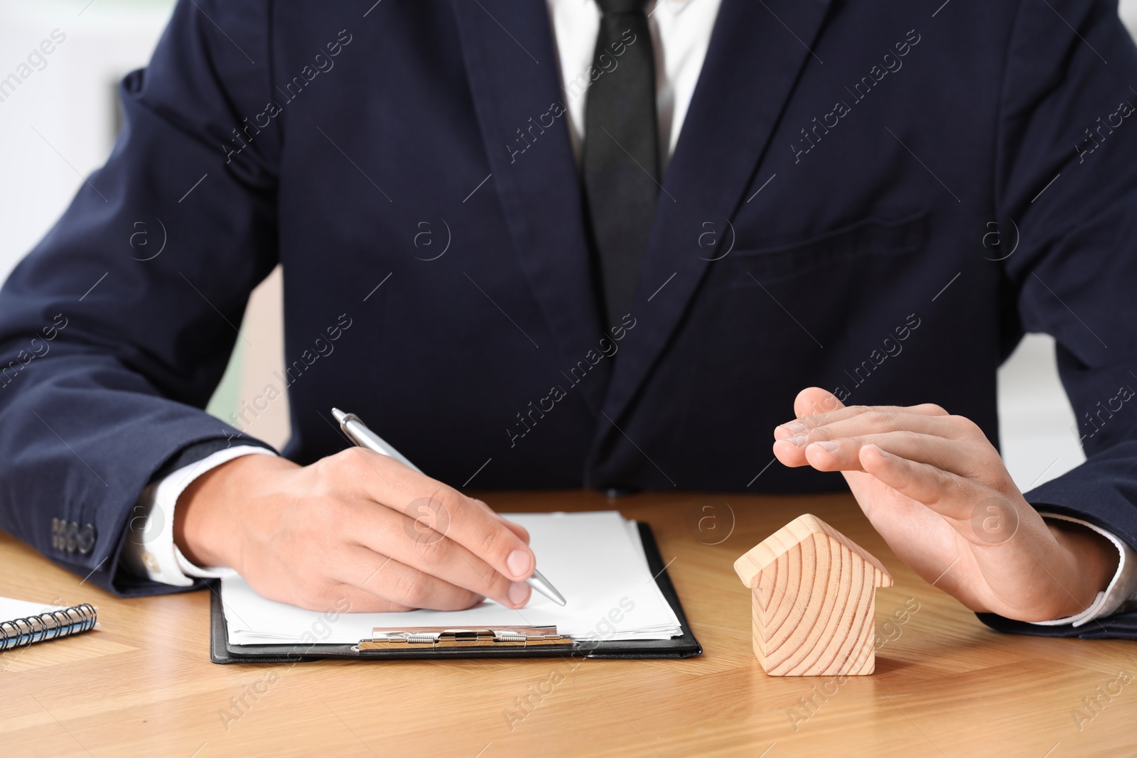 Photo of Property insurance. Real estate agent protecting house figure while working at wooden table, closeup