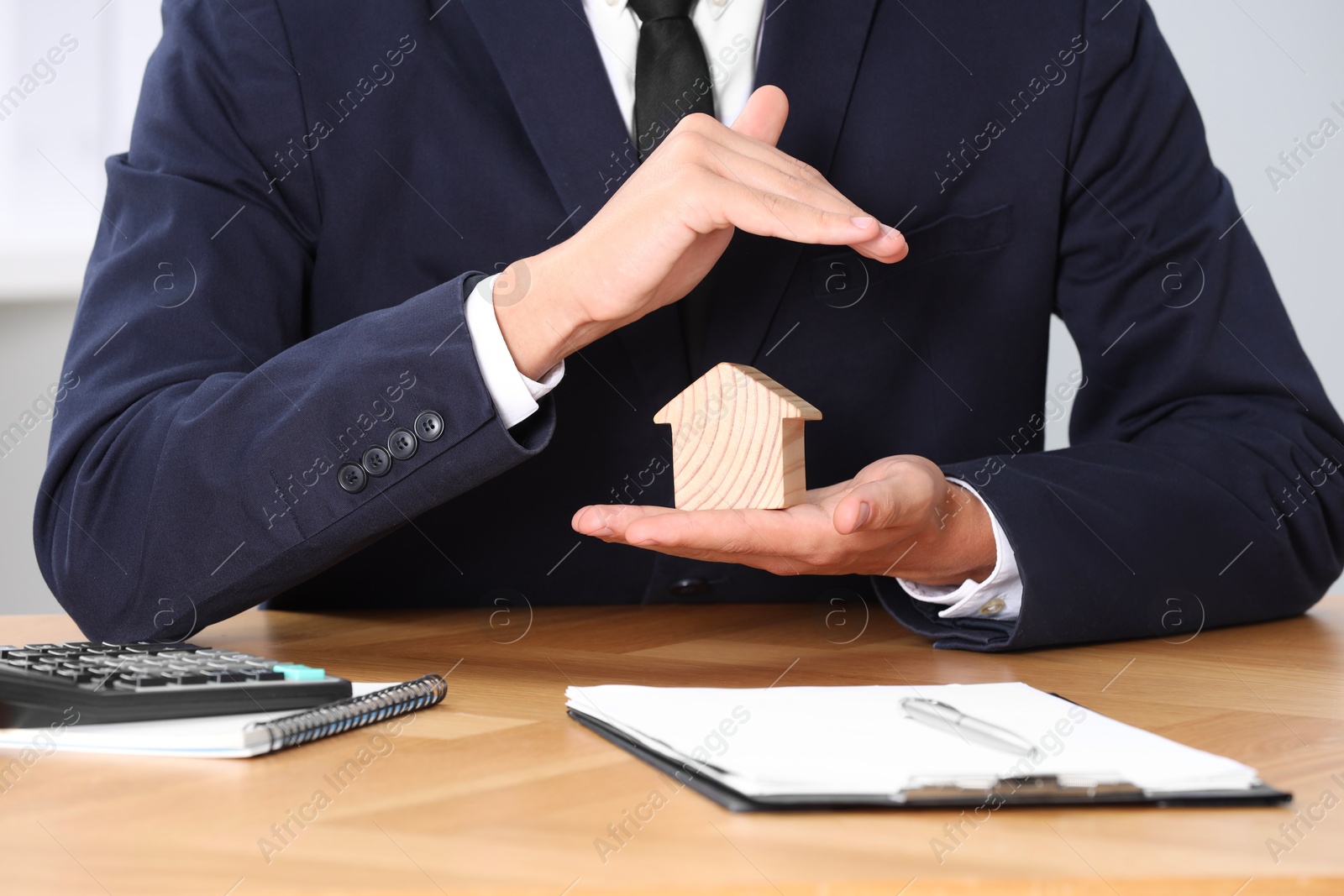 Photo of Property insurance. Real estate agent protecting house figure at wooden table, closeup